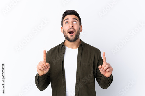 Young handsome man with beard over isolated white background surprised and pointing up