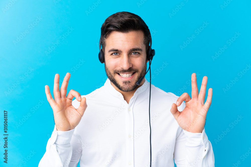 Naklejka premium Telemarketer man working with a headset over isolated blue background showing an ok sign with fingers
