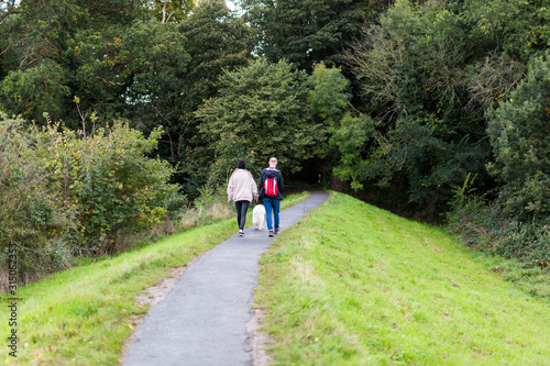 A couple taking their dog for a walk along a path leading into a wooded area