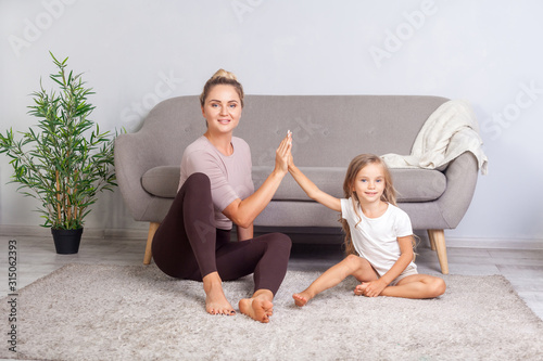 Fit attractive woman giving high five to happy little daughter, teamwork concept, mother and child sitting on floor taking break relaxing after sport fitness, resting together. trust to teammate photo