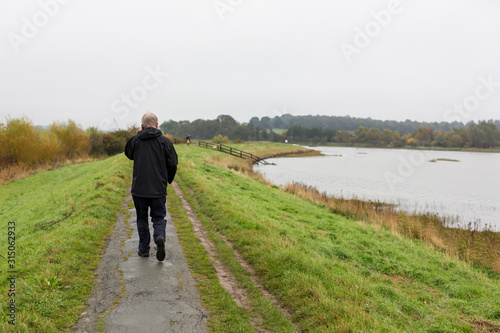 A middle aged man walking along a river path while talking on his mobile phone