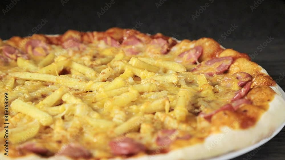 close-up of a pizza with cheese tomatoes, sausage and egg that revolves around itself on a black background view from the top close-up of a pizza with cheese tomatoes, sausage and egg that revolves around itself on a black background view from the top