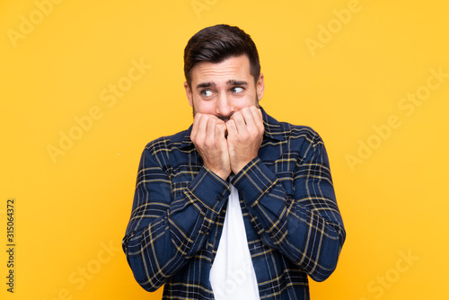 Young handsome man with beard over isolated yellow background nervous and scared putting hands to mouth photo