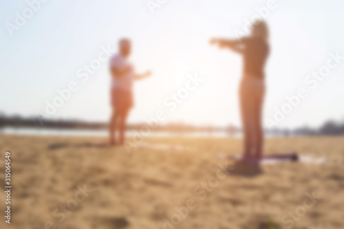 A man practices yoga with a woman on the riverbank. Golden sand, background, blurred © HENADZY