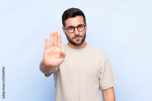 Fotografía Young handsome man with beard over isolated blue background making stop gesture