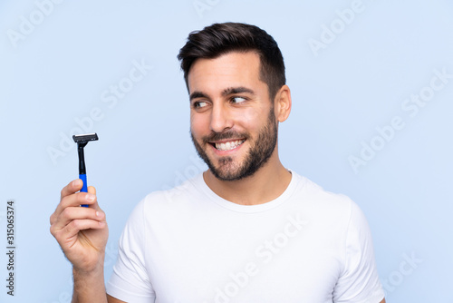 Young handsome man shaving his beard over isolated background with happy expression