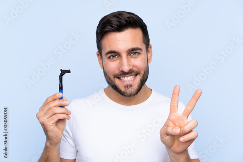 Young handsome man shaving his beard over isolated background smiling and showing victory sign