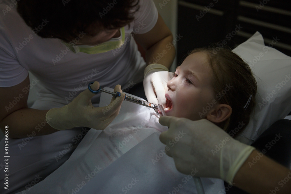 Scared little girl at dentist office, getting local anesthesia injection into gums, dentist