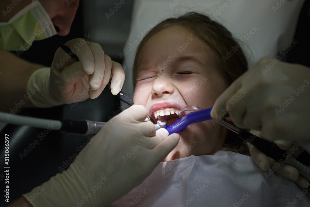Scared little girl at the dentists office, in pain during a treatment.