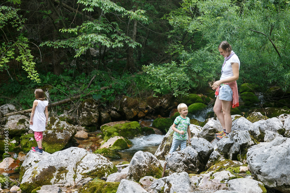 Mother with children having fun, playing by a mountain creek in summer.