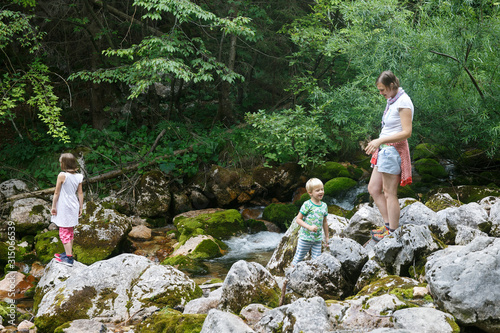 Obraz na płótnie Mother with children having fun, playing by a mountain creek in summer. w salonie