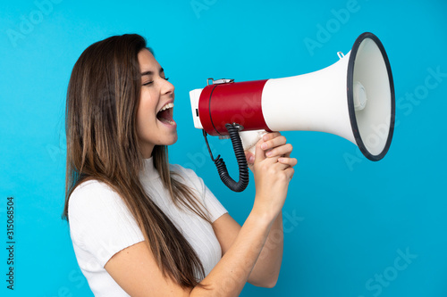 Fényképezés Teenager girl over isolated blue background shouting through a megaphone
