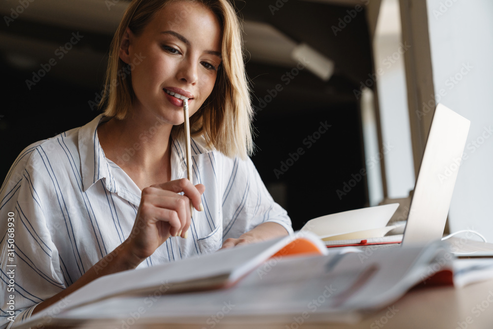 Photo of focused pleased woman making notes and using laptop