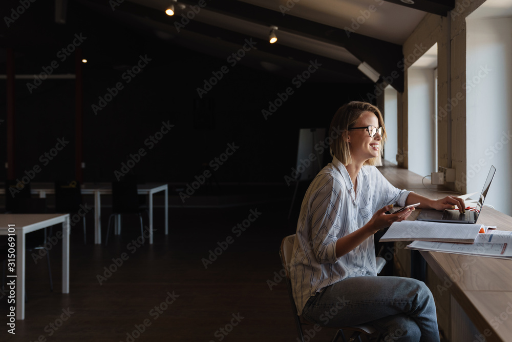 Photo of smiling caucasian woman using mobile phone and laptop