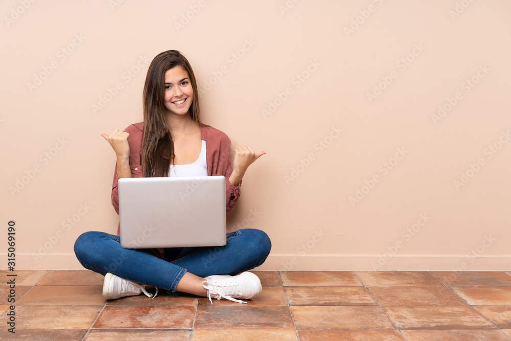 Teenager student girl sitting on the floor with a laptop with thumbs up gesture and smiling Teenager student girl sitting on the floor with a laptop with thumbs up gesture and smiling