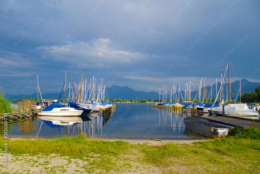 A small harbor on a Chiemsee lake (Bavaria, Germany) on a calm, beautiful and sunny summer day. Several sailboats are parked on two piers. Day is quite cloudy.