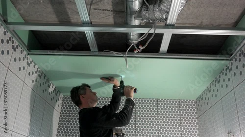 Worker is fixing drywall to ceiling profiles with screwdriver. handheld