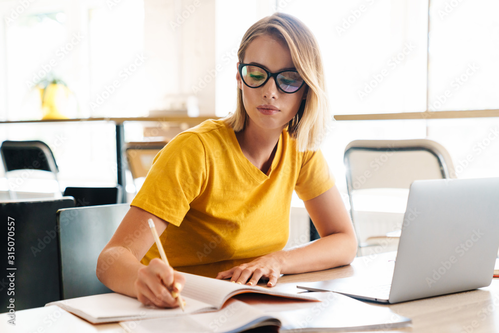 Photo of beautiful young woman making notes and using laptop Photo of beautiful young woman making notes and using laptop