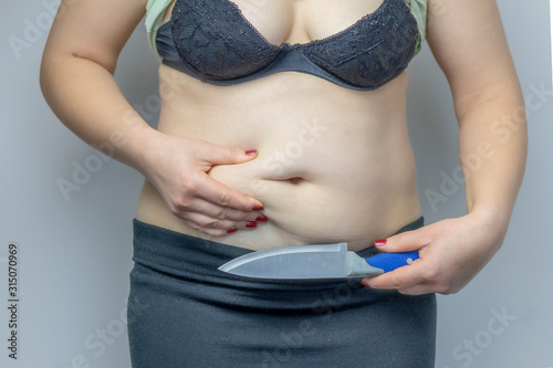 Woman in a black bra. Holds a knife near the abdomen. Close-up. On white background. The concept wants to cut excess weight photo