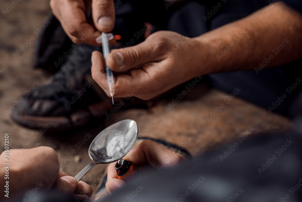 two shabby  men preparing drug injection in slums