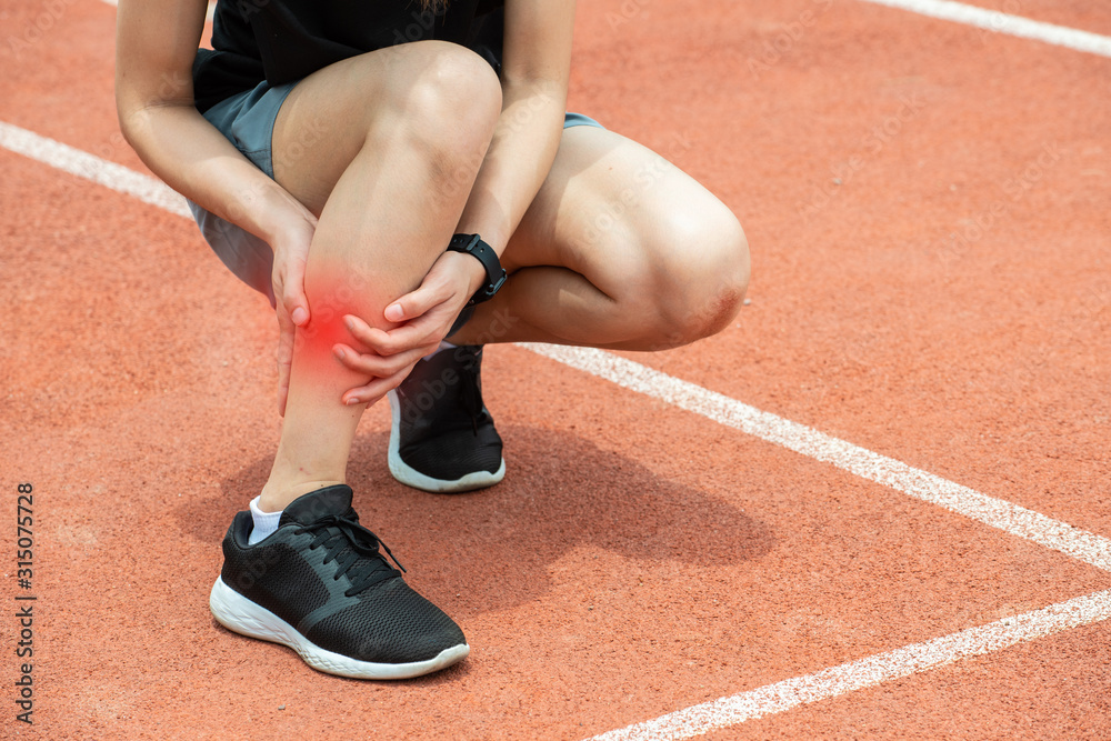 Close up of runner woman holding her calf, suffering from calf pain after running. Conceptual of injury from running workout.