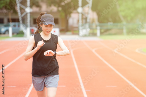 Portrait of young athlete runner woman running in the running track and she looking to her smart watch. Running track is a rubberized artificial running surface for track and field athletics. © boyloso