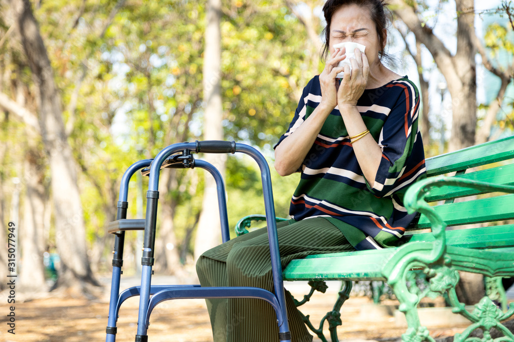 Sick asian senior woman sneezing in a tissue blowing her runny nose,female elderly suffer from allergic rhinitis,weather is changing,seasonal virus infection,old people with allergy in nature outdoor Sick asian senior woman sneezing in a tissue blowing her runny nose,female elderly suffer from allergic rhinitis,weather is changing,seasonal virus infection,old people with allergy in nature outdoor