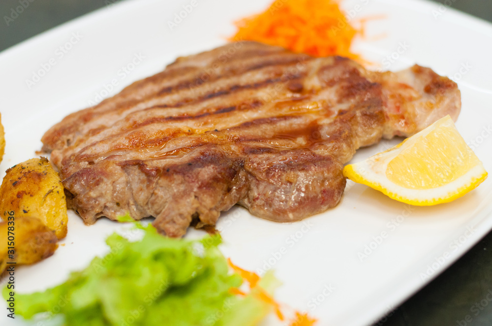 Juicy and delicious grilled meat steak with lemon, carrots, lettuce and potatoes.