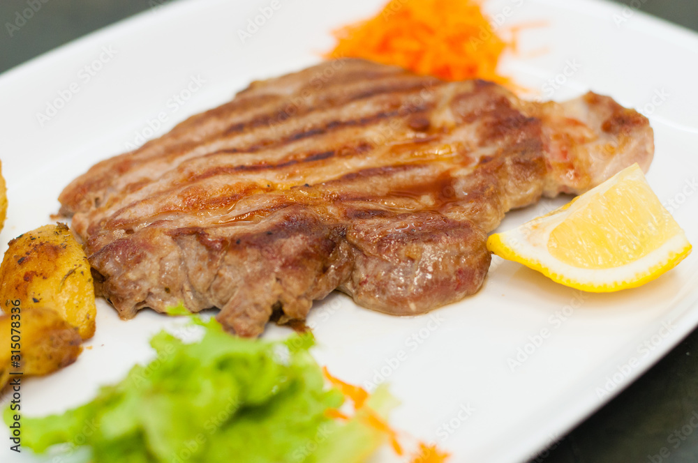 Juicy and delicious grilled meat steak with lemon, carrots, lettuce and potatoes. Juicy and delicious grilled meat steak with lemon, carrots, lettuce and potatoes.