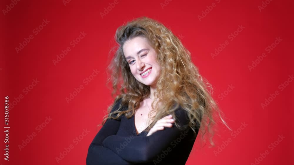 Red-haired girl with curly long hair on a red background. Black blouse, flirts, smiles, gets upset with braces and winks. Red-haired girl with curly long hair on a red background. Black blouse, flirts, smiles, gets upset with braces and winks.