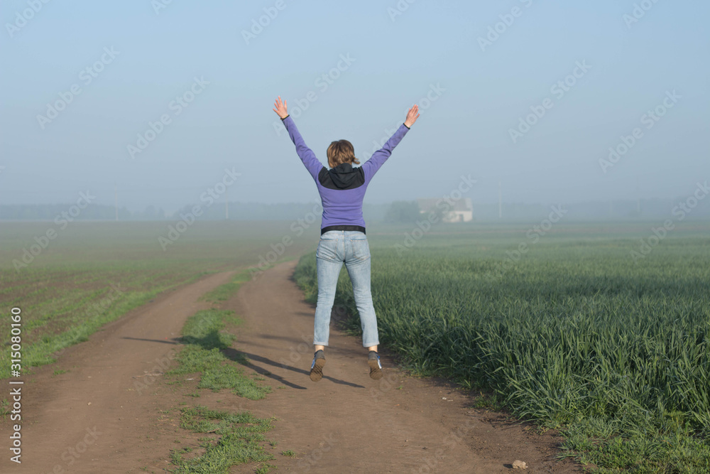 Fototapeta premium Happy woman traveler jumps among fields beautiful misty morning