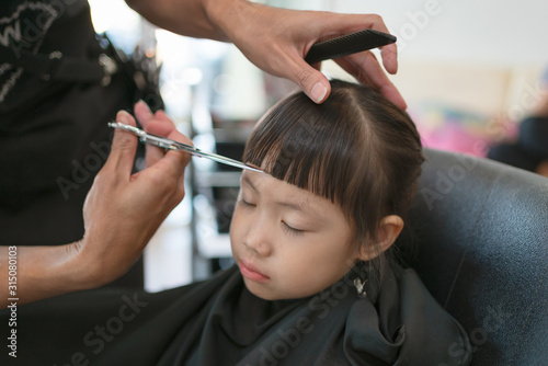 Little girl getting haircut by hairdresser at the barbershop.