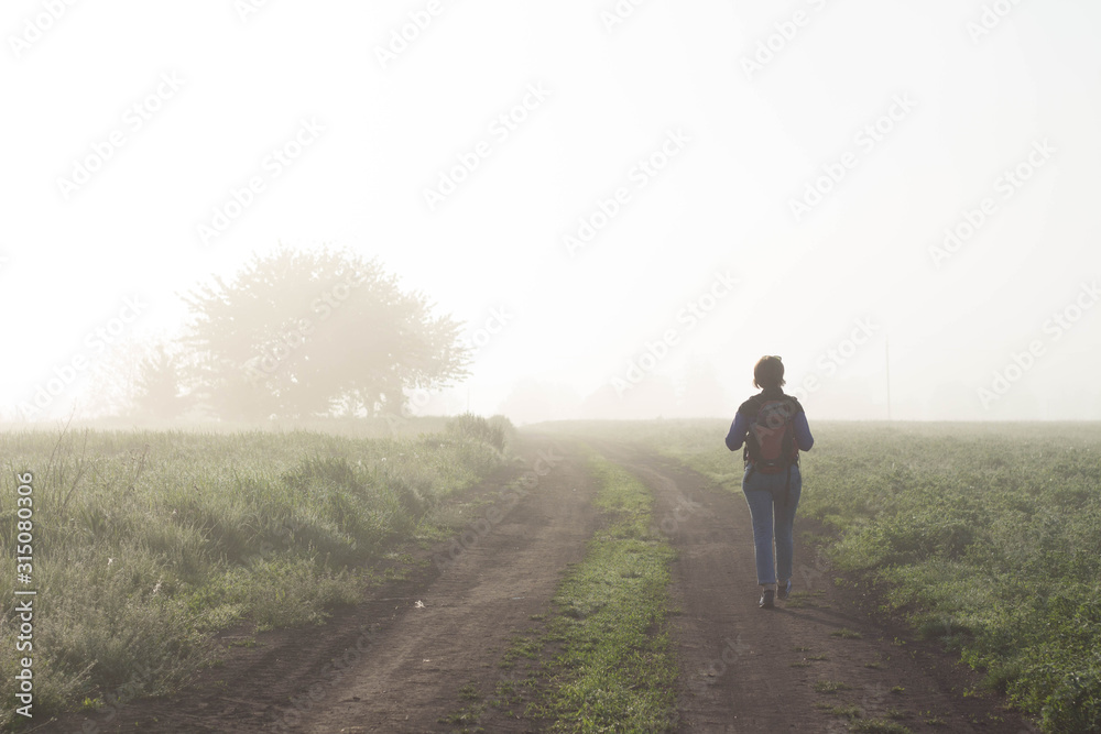 Back view of a woman traveler who walks in nature very beautiful atmospheric misty morning