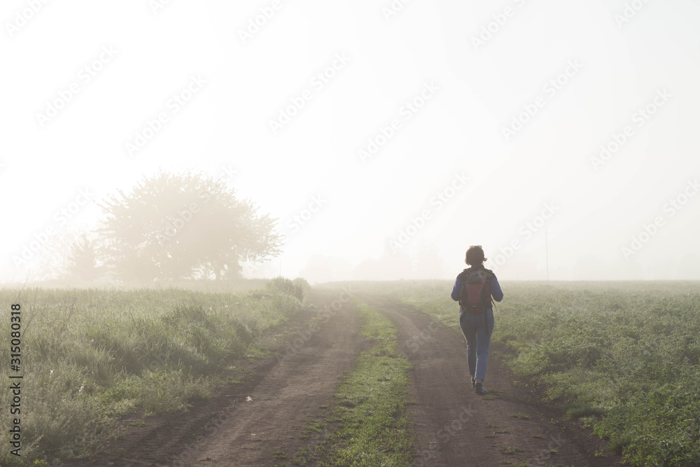 Back view of a woman traveler who walks in nature very beautiful atmospheric misty morning