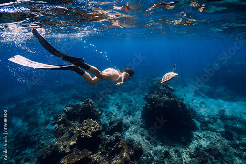 Freediver with fins glides underwater with turtle in ocean. Snorkeling with sea turtle.