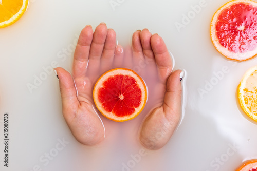 Red grapefruit in hands. Slice of yellow oranges and grin lime citrus fruits in murky muddy milky water.