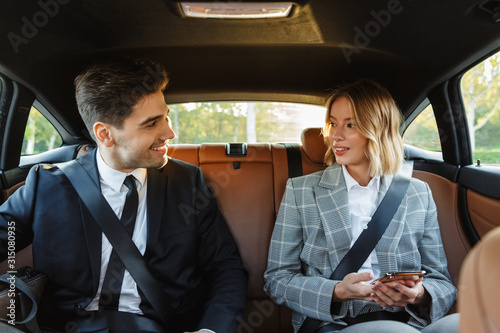 Image of young businesslike man and woman in formal wear sitting in car