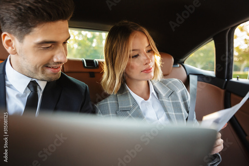 Image of businesslike man and woman sitting in car with working documents