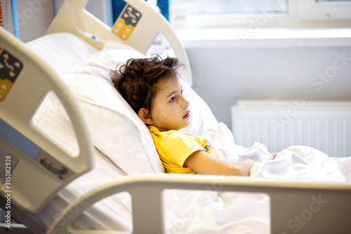 7 years old ill child in yellow t-shirt lying in hospital bed after serious nasal surgery. Medical care for children. Healthcare in clinic after surgery. Little girl in hospital bed