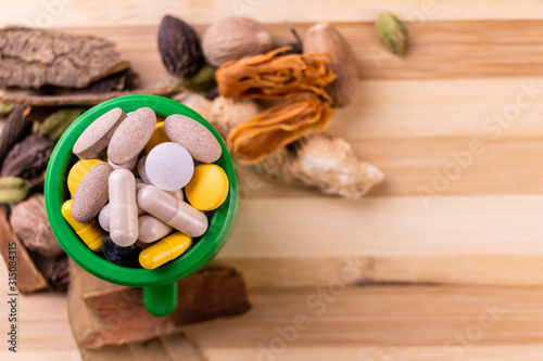 Top view macro shot of herbal pills and tablets arranged with spices on a red stone. Unani medicines concept.