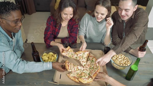 Happy multiethnic friends drinking beer, eating pizza and having fun together in the living room at home