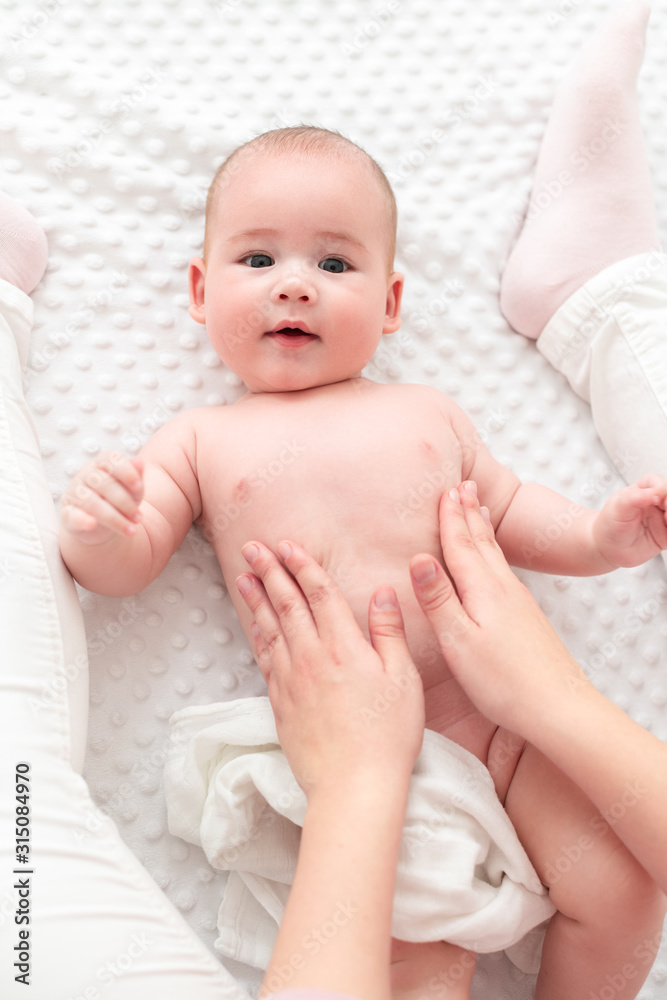 Baby massage. Female therapist gently massaging newborn baby boy. Mother applying body lotion to her infant baby boy. Newborn massage top view background.