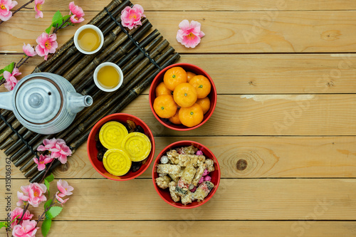 Table top view Lunar New Year & Chinese New Year vacation concept background.Flat lay orange in wood basket & pink cherry blossom with red pocket money & decorations on modern rustic brown backdrop