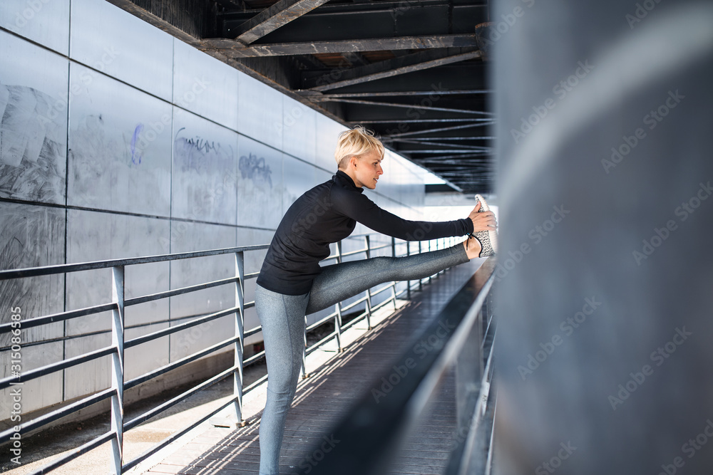 Fototapeta premium A portrait of young sportswoman doing exercise outdoors, stretching.