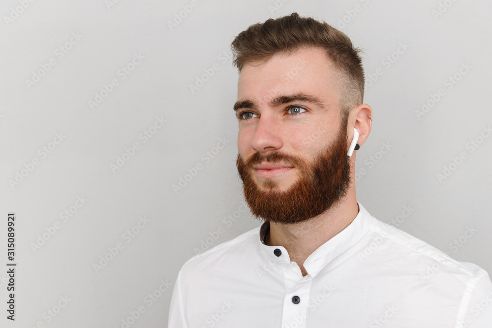 Image of young handsome man with beard posing and using earpod Image of young handsome man with beard posing and using earpod