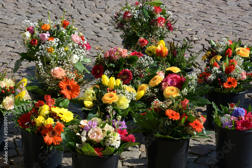 mixed bunches of spring flowers in basket outdoors, bouquet of different flowers selling in a market on paving stones