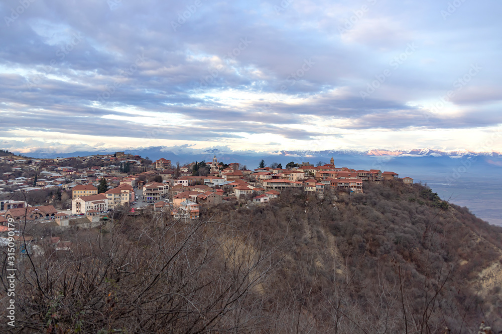 View of Sighnaghi city standing on a hill against the backdrop of snow-capped mountains and sky in clouds. Georgia