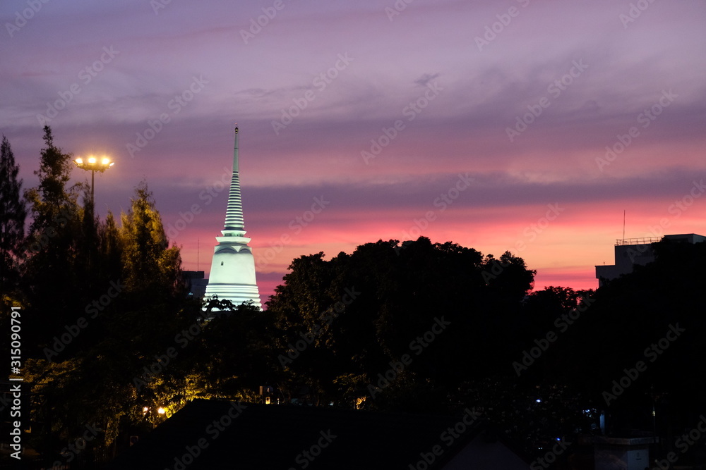 Beautiful sunset over the silhouettes of trees. Lighted spire of a Buddhist temple.