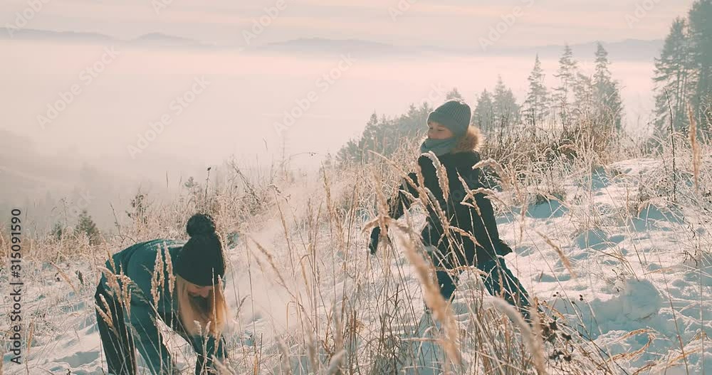 Family winter holiday, mother and child having fun running between snow trees in winter forest, beautiful snow landscape. Travel together concept.