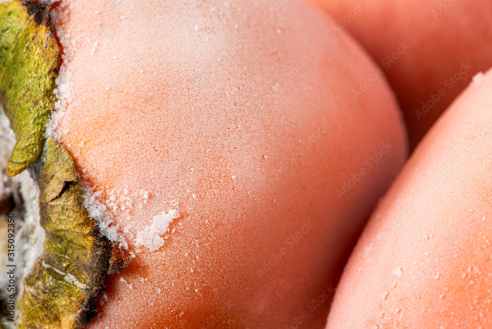 Fototapeta premium Large ripe frozen persimmons closeup. Persimmon fruit is covered with hoarfrost.
